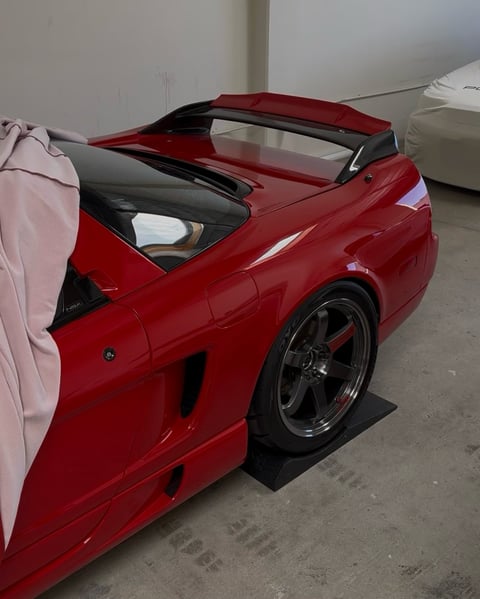 Red sports car with retractable hardtop roof open, displayed in garage with custom black accents and performance wheels
