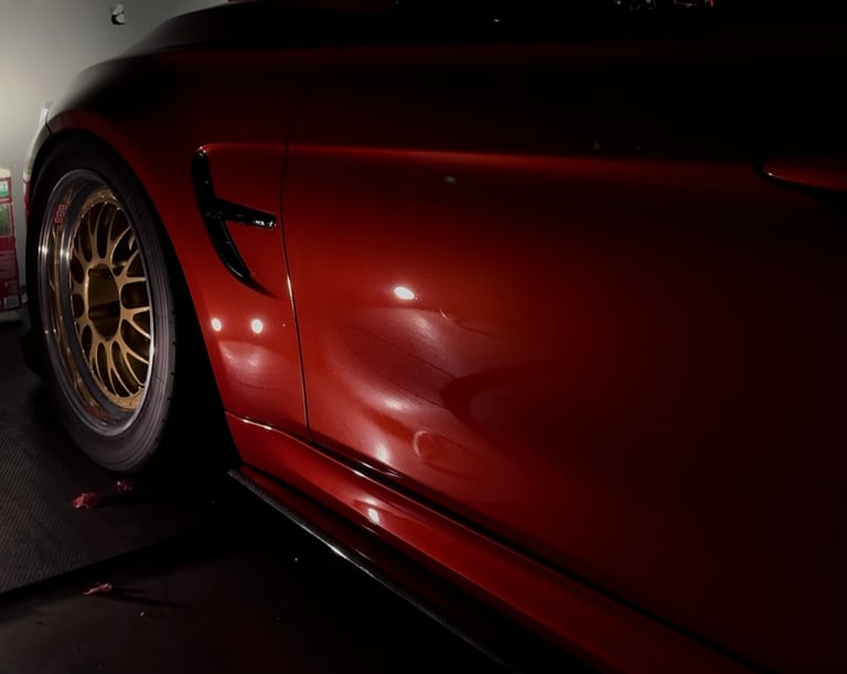 Red sports car side profile showing gold-colored wheel and door panel with visible dents