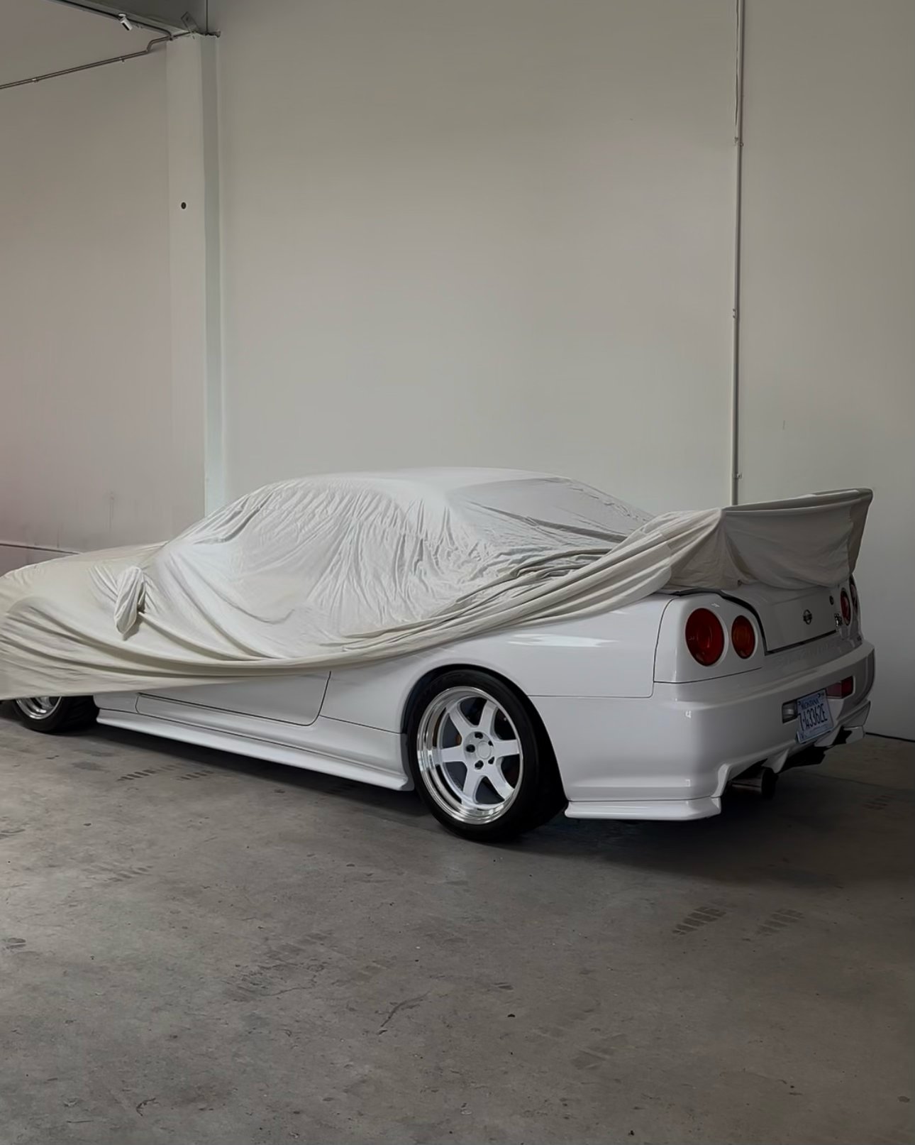 White sports car covered with a protective cloth cover in an indoor garage