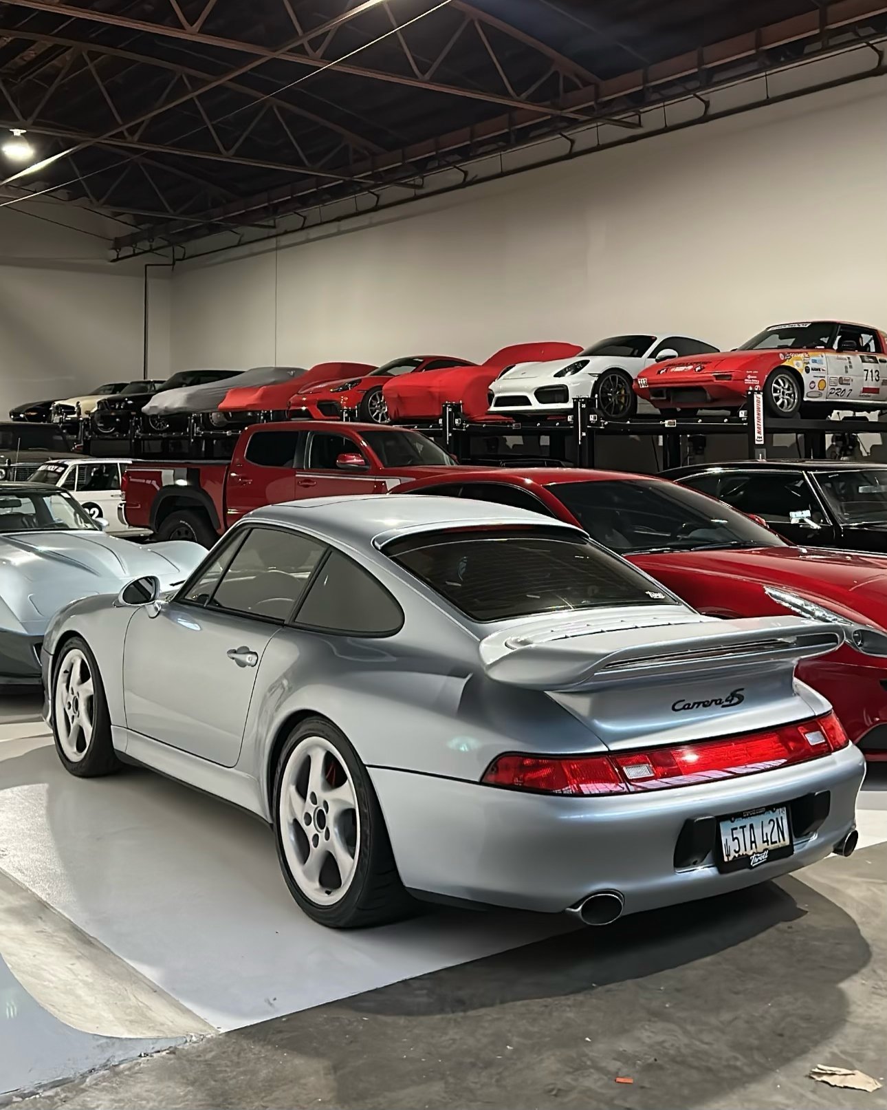 Silver Porsche 911 Carrera displayed in a car showroom with red sports cars visible in the background
