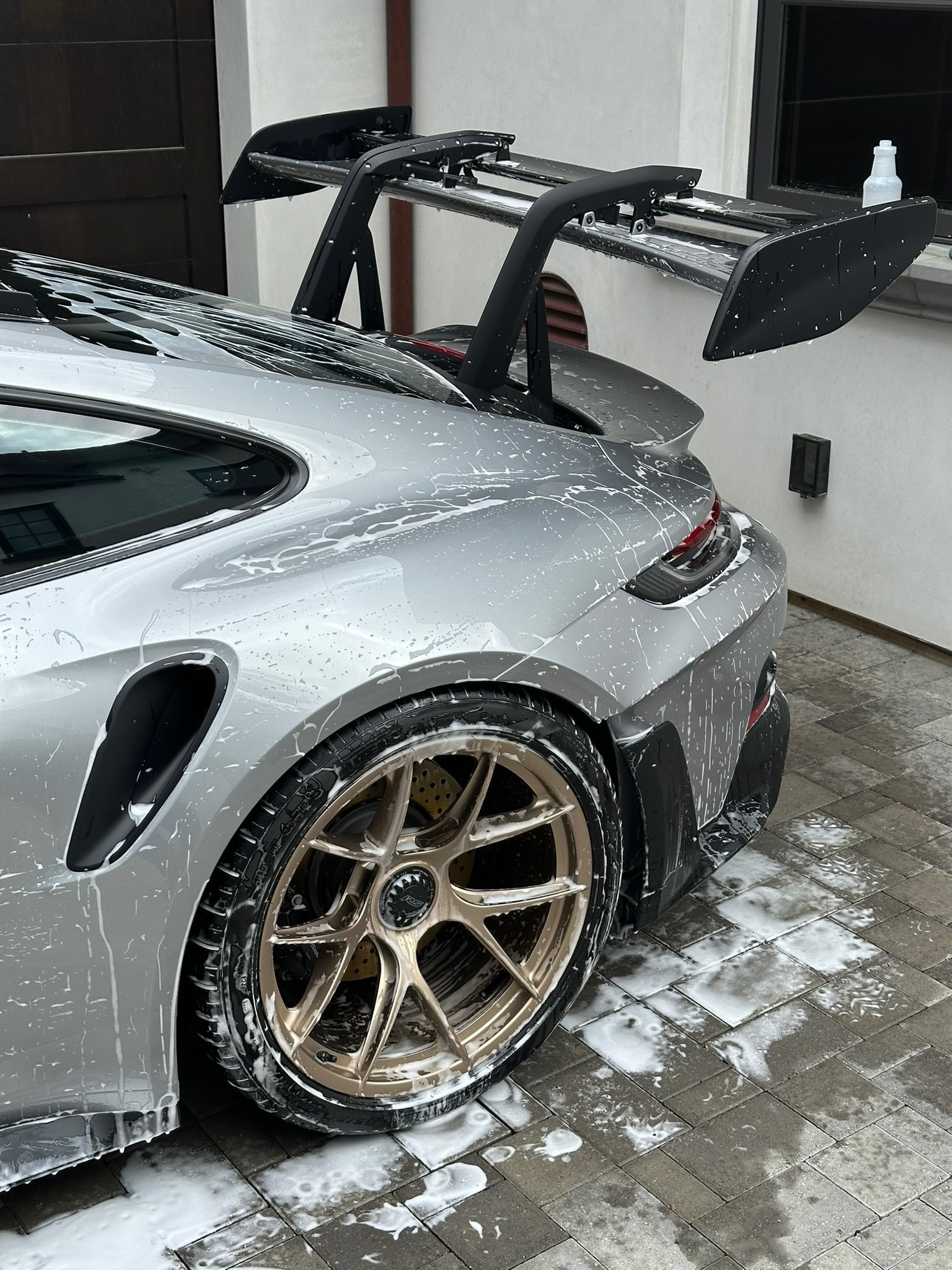 Silver sports car with black roof rack and bronze alloy wheels in garage, wet pavement visible