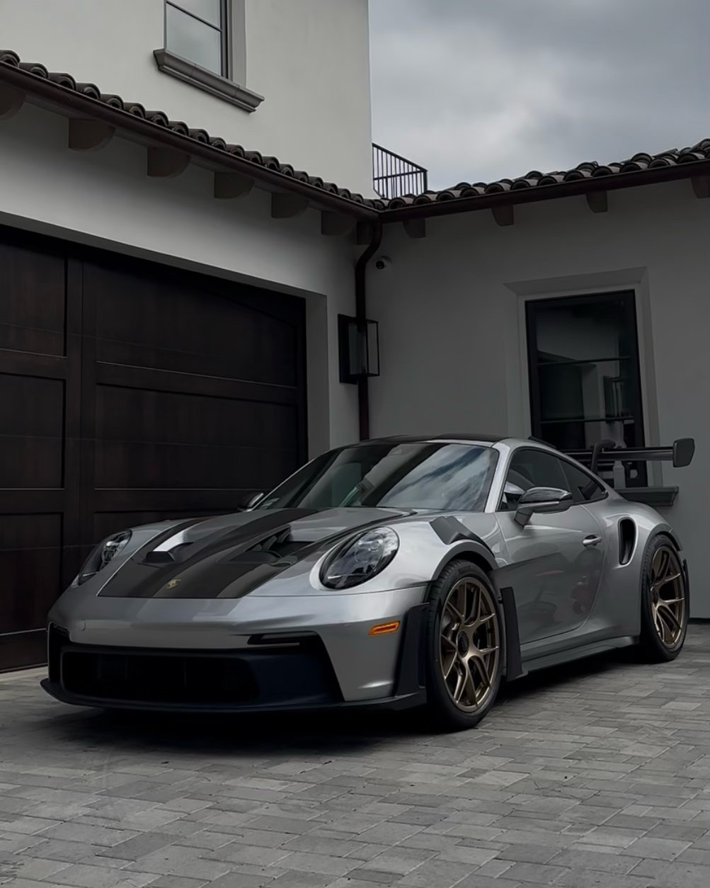 Silver Porsche 911 GT2 RS sports car parked in front of modern white villa with black garage doors