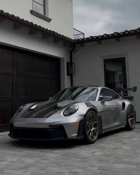 Silver Porsche 911 GT2 RS sports car parked in front of modern white villa with black garage doors