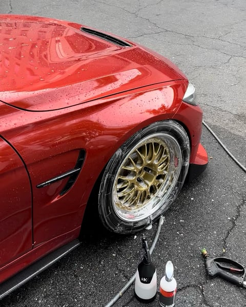Close-up of red sports car with gold alloy wheel and car detailing products on asphalt surface
