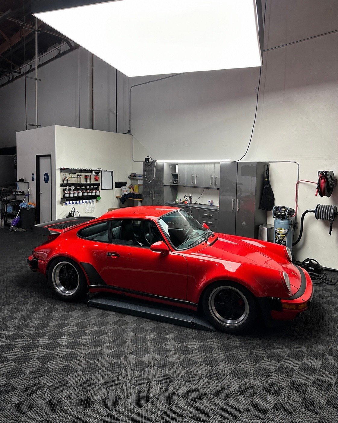Red vintage Porsche 911 parked in a modern automotive workshop with workbench and overhead lighting