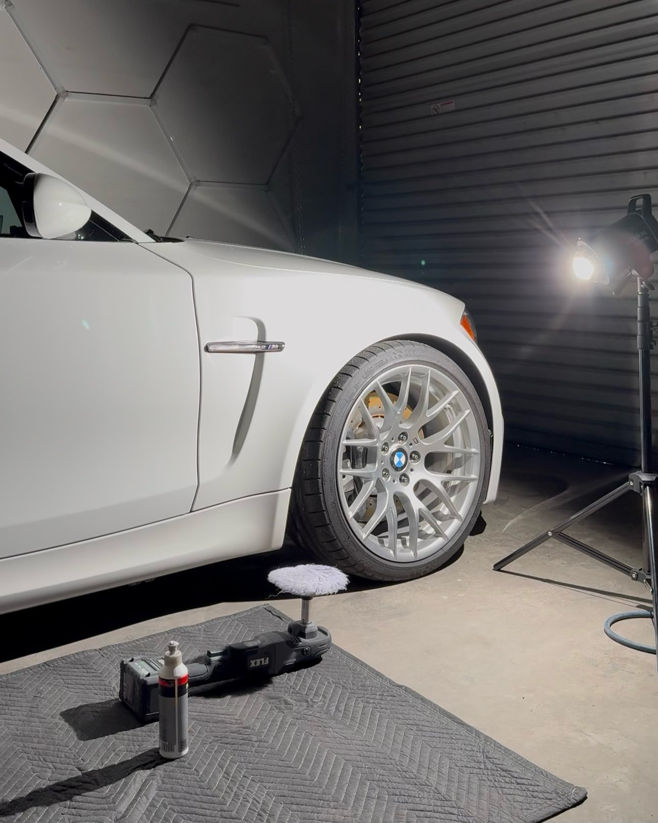 White car with silver wheel supported by jack on floor in professional garage workshop with lighting