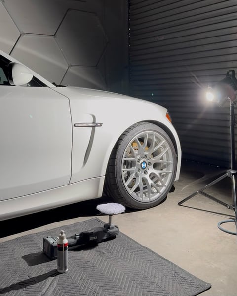 White car with silver wheel supported by jack on floor in professional garage workshop with lighting