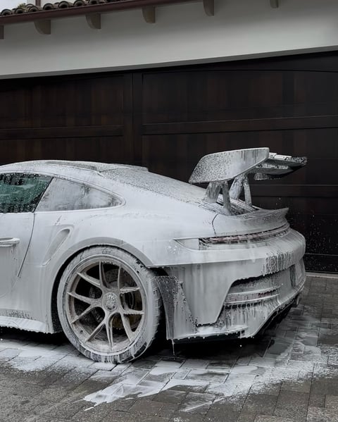 White Porsche sports car covered in ice and snow in a driveway with black garage doors in the background