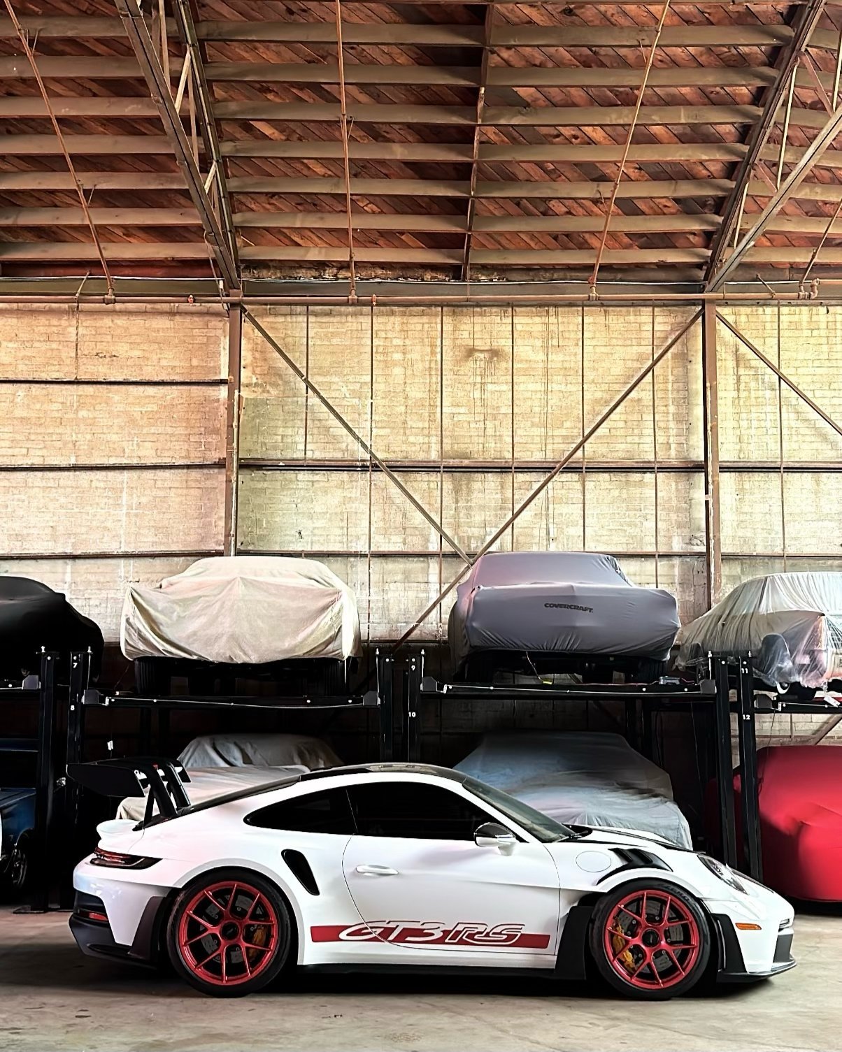 White Porsche 911 GT2 RS sports car with red wheels parked in a garage with vehicle lifts and storage