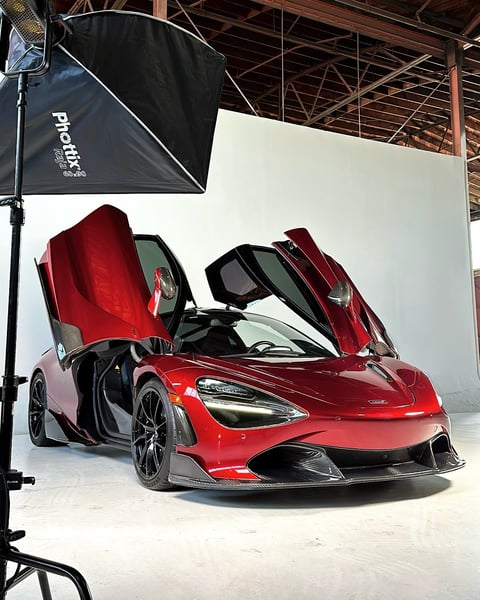 Red sports car with open gull-wing doors displayed in a studio setting with professional lighting