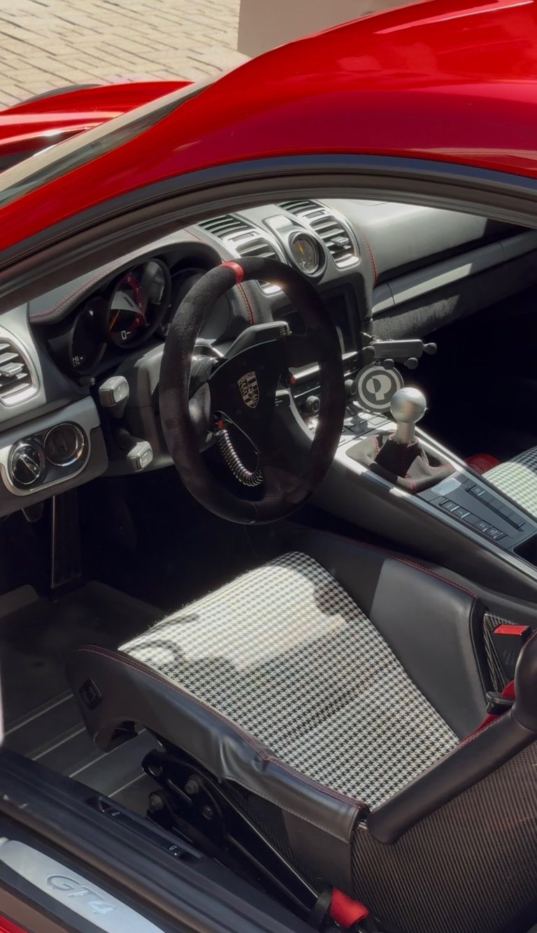 Interior of red sports car with black steering wheel, white and gray dashboard, and checkered pattern seat cover